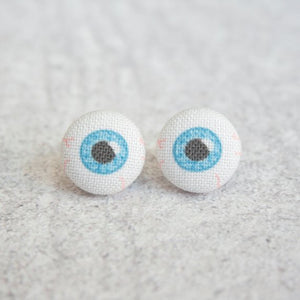 Two round earrings made out of fabric depicting eyeballs. There are blue irises, black pupils, and faint red veins.