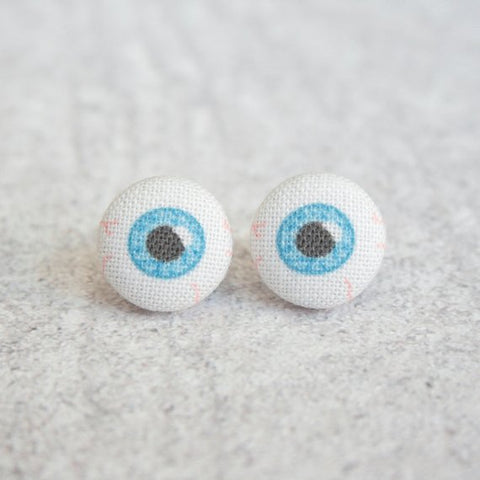 Two round earrings made out of fabric depicting eyeballs. There are blue irises, black pupils, and faint red veins.