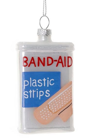 A white glass ornament of a box with Band-Aid in red letters and a beige bandage over a blue square.