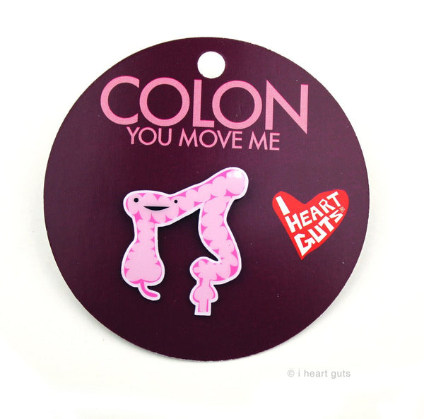 A maroon background with a pink enamel pin depicting a colon with two eyes and a smile.