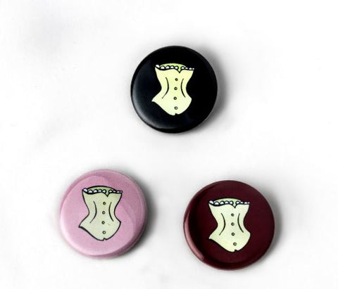 Three round buttons in pink, maroon, and black, with a photo of a white corset on it.
