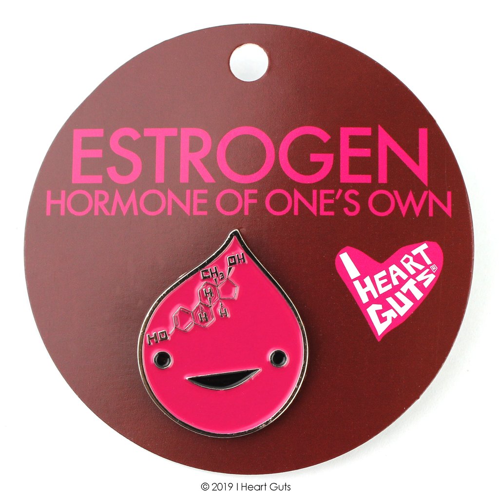 A maroon card with "Estrogen Hormone of One's Own" written in pink letters. An red enamel pin with two black eyes and smile and the chemical breakdown of estrogen sits on the card.