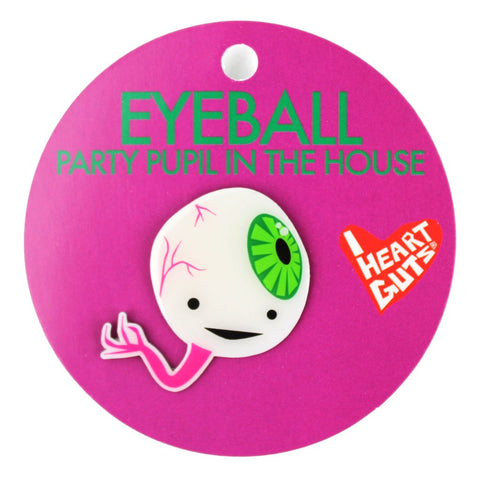 A pink card with "Eyeball Party Pupil in the House" written with green letters. There is an enamel pin depicting an eyeball with two eyes and a smile. It has a green iris, pink veins, and a large pink vein coming out of it.
