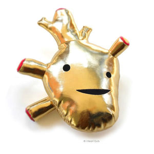 A gold vinyl plush with two eyes and a smile in the shape of an anatomical heart.