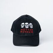 A black baseball hat with three different white skulls embroidered on it. The Mütter Museum logo in red is embroidered underneath it.