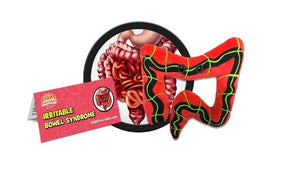 A red plush in the shape of an intestine. There is a stripe of black and yellow running through the middle and there are two black eyes. There is a card that reads "Irritable Bowel Syndrome" next to it. 