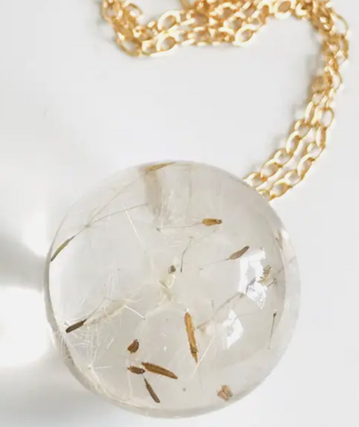 A gold chain with a sphere of resin with dandelion puffs encase inside.