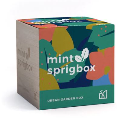 A wood box with a colorful cover with "Mint Sprigbox Urban Garden Box" written on it.