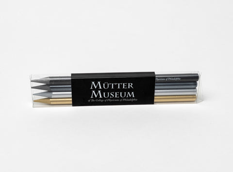 A plastic case containing four different graphite pencils; silver, gold, grey, and black. There is a black label on the front with the Mütter Museum logo.