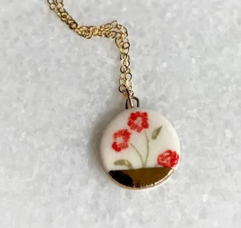 Red flowers with green stems on a clay circle pendant, dipped in gold at the base, on a gold chain.
