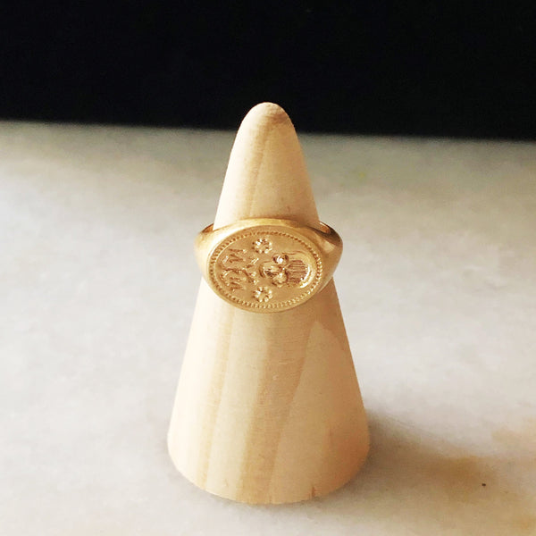 A brass ring with an impression of an antique wax mold depicting a skull with the letters MM and flowers on it.