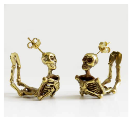 Two curved skeleton earrings with their hands across their chest. They are brass and face each other.