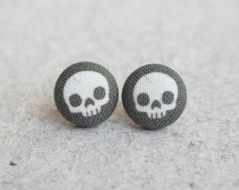 Black fabric stud earrings in the shape of a circle with a white skull on them.