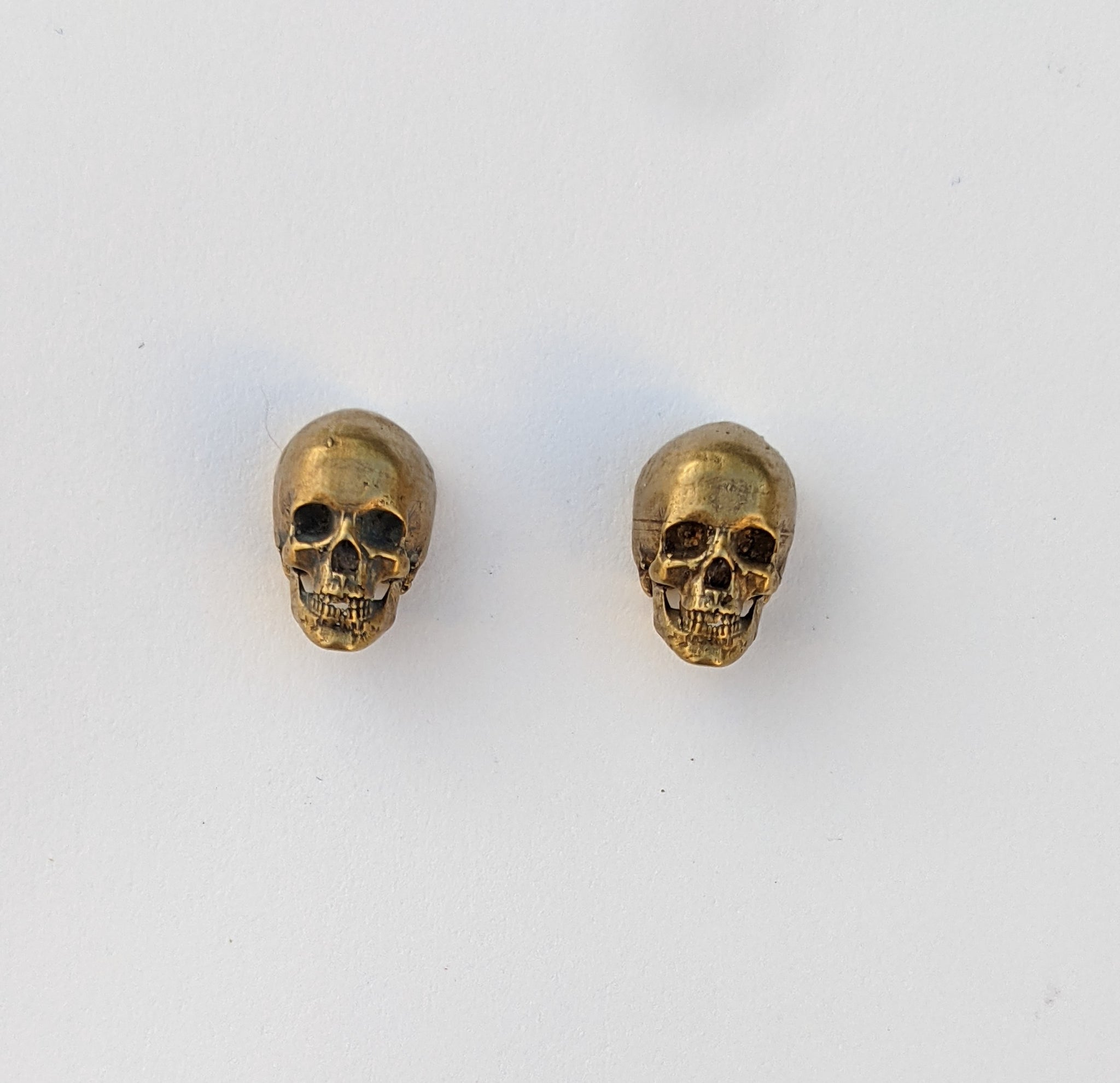 A pair of matching skull earrings with detailed eyes, nose, jaws, and teeth in yellow bronze.